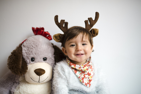 Portrait of happy baby girl with reindeer antlers headband beside her toy dog stock photo