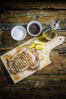 Gebratenes Beefsteak mit Rosmarin und Zitrone auf Schneidebrett, Salz, Pfeffer und Olivenöl - GIOF03701