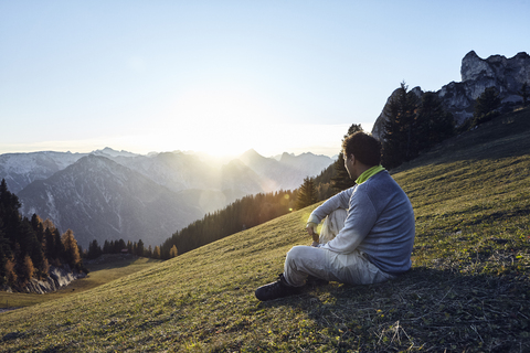 Österreich, Tirol, Rofangebirge, Wanderer sitzt bei Sonnenuntergang auf einer Wiese, lizenzfreies Stockfoto