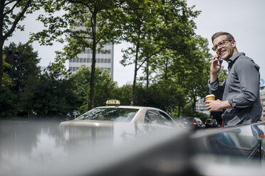 Smiling young businessman with coffee to go on the phone - KNSF03249