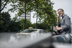 Lächelnder junger Geschäftsmann mit Kaffee zum Mitnehmen am Telefon - KNSF03249