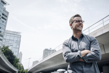 Portrait of laughing young businessman with arms crossed outdoors - KNSF03252