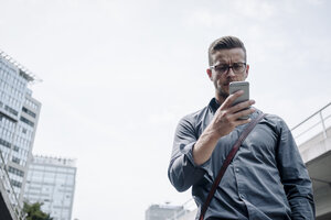 Porträt eines ernsten jungen Geschäftsmannes, der auf sein Smartphone schaut - KNSF03253