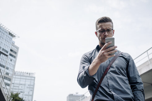 Portrait of serious young businessman looking at smartphone - KNSF03253