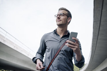 Portrait of smiling young businessman with smartphone - KNSF03255