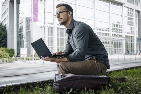 Young businessman sitting outdoors using laptop - KNSF03262