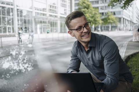 Portrait of laughing young businessman with laptop outdoors stock photo