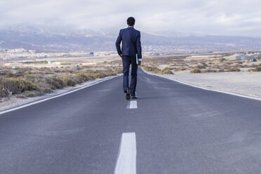 Spain, Tenerife, young businessman with laptop walking on road - SIPF01893