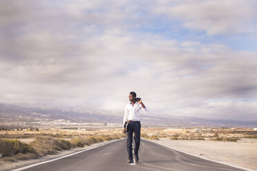 Spain, Tenerife, young businessman with skateboard walking on road - SIPF01901