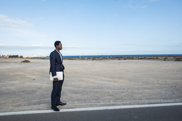 Spain, Tenerife, young businessman with laptop standing on road - SIPF01905