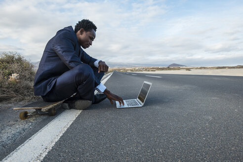 Spanien, Teneriffa, junger Geschäftsmann auf Skateboard sitzend und mit Laptop - SIPF01907
