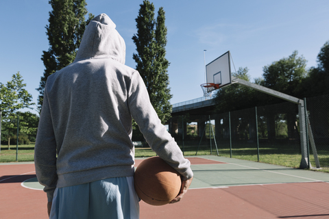 Mann hält Basketball, Basketballkorb im Hintergrund, lizenzfreies Stockfoto