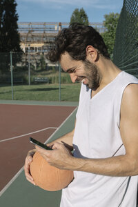 Basketballspieler schaut auf sein Smartphone und lächelt - ALBF00336