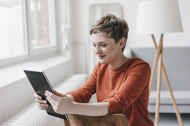 Smiling woman sitting on chair using tablet - KNSF03268