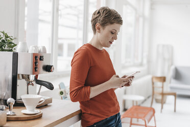 Frau benutzt Mobiltelefon an Kaffeemaschine - KNSF03276