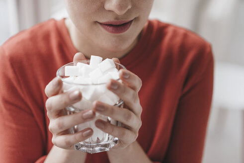 Close-up of woman holding glass full of sugar cubes - KNSF03279