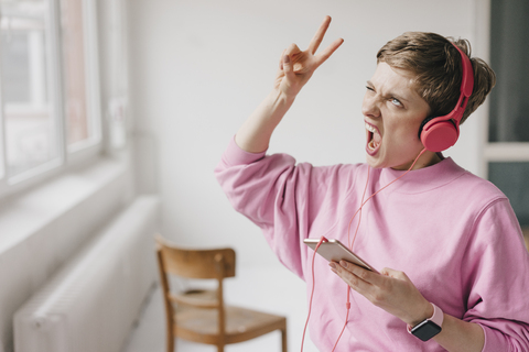 Frau mit Mobiltelefon und Kopfhörern posiert beim Musikhören, lizenzfreies Stockfoto