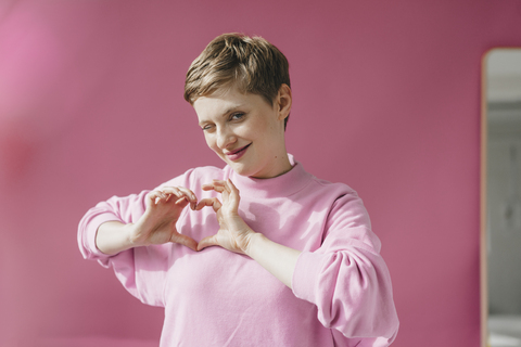 Porträt einer Frau in Rosa, die mit ihren Händen ein Herz formt, lizenzfreies Stockfoto