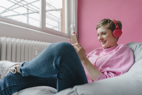 Lächelnde Frau im Sitzsack mit Handy und Kopfhörern, lizenzfreies Stockfoto