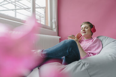 Smiling woman in beanbag with cell phone and headphones listening to music - KNSF03303