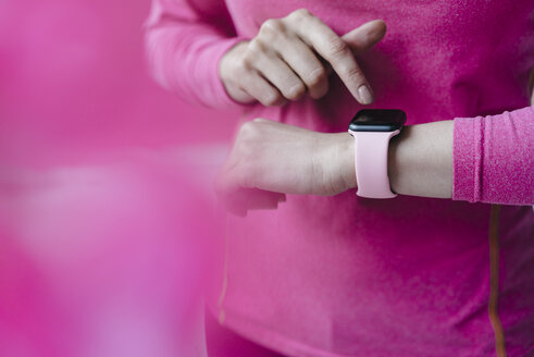 Nahaufnahme einer Frau in rosa Sportkleidung, die ihre Smartwatch einstellt - KNSF03316