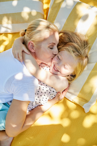 Glückliches Mädchen und Mutter umarmen und küssen sich auf einer Decke, lizenzfreies Stockfoto