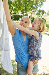 Happy girl and mother hanging the laundry on clothesline - SRYF00608