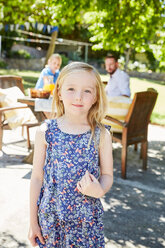 Porträt eines lächelnden Mädchens mit Eltern im Hintergrund am Gartentisch - SRYF00620