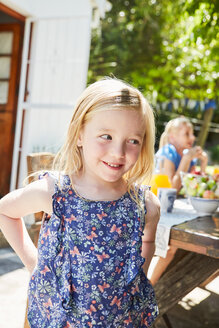 Porträt eines lächelnden Mädchens mit Mutter im Hintergrund am Gartentisch - SRYF00622