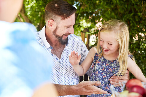 Glückliches Mädchen mit Vater am Gartentisch sitzend, High Fiving - SRYF00628