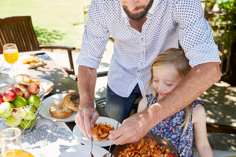 Father dishing up pasta for daughter at garden table stock photo