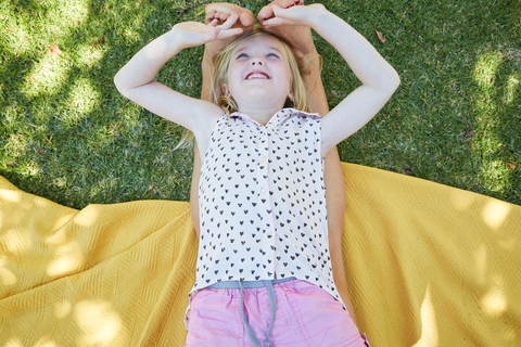 Glückliches Mädchen auf einer Decke liegend und mit den Füßen der Mutter spielend, lizenzfreies Stockfoto