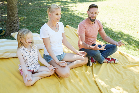 Familie mit Mädchen übt Yoga auf einer Decke, lizenzfreies Stockfoto