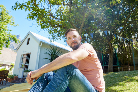 Porträt eines bärtigen Mannes, der vor einem Haus sitzt, lizenzfreies Stockfoto