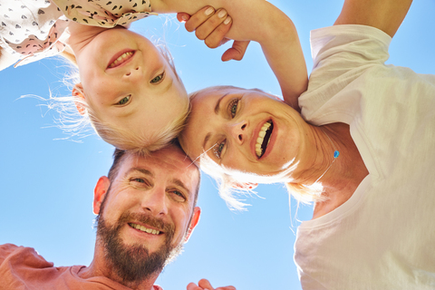Porträt einer glücklichen Familie, die unter blauem Himmel kauert, lizenzfreies Stockfoto