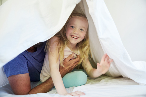 Happy girl with father in bed under blanket stock photo