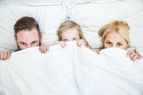 Portrait of family lying in bed hiding under blanket stock photo