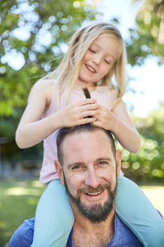 Happy girl sitting on father's shoulders doing his hair stock photo