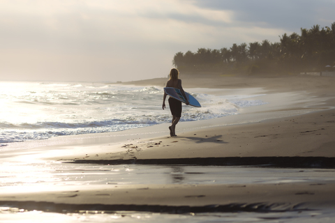 Indonesien, Bali, junger Surfer geht am Strand spazieren, lizenzfreies Stockfoto