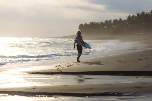 Indonesien, Bali, junger Surfer geht am Strand spazieren - KNTF00933