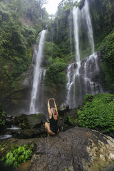 Indonesien, Bali, junge Frau hockt am Wasserfall - KNTF00936