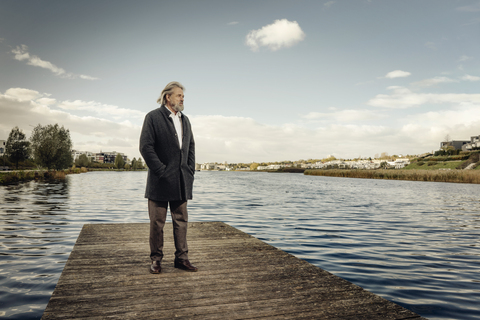 Älterer Mann steht auf einem Steg an einem See, lizenzfreies Stockfoto