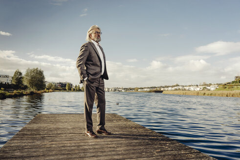 Senior man standing on jetty at a lake - KNSF03328