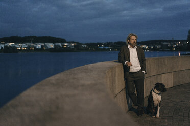 Älterer Mann mit Hund am Seeufer am Abend stehend - KNSF03335
