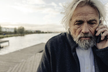 Portrait of serious senior man on cell phone at a lake - KNSF03339