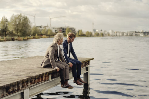 Zwei Geschäftsleute sitzen auf einem Steg an einem See - KNSF03344