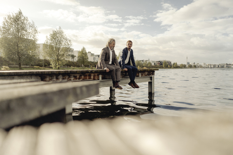 Two businessmen sitting on jetty at a lake stock photo