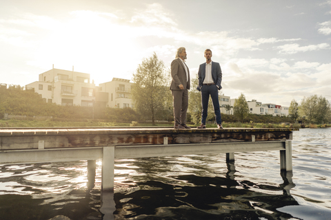 Zwei Geschäftsleute stehen auf einem Steg an einem See, lizenzfreies Stockfoto