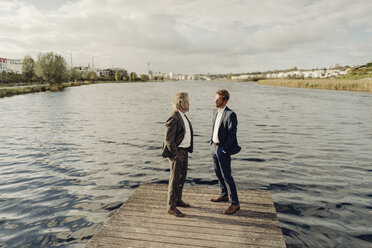 Zwei Geschäftsleute stehen auf einem Steg an einem See und unterhalten sich - KNSF03350