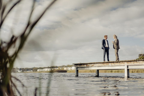 Zwei Geschäftsleute stehen auf einem Steg an einem See und unterhalten sich, lizenzfreies Stockfoto
